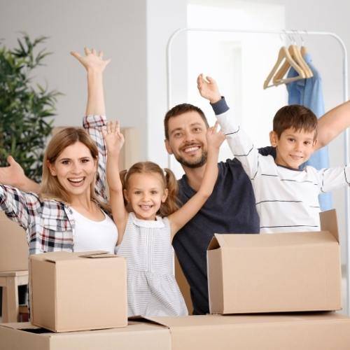 Famille heureuse entourée de cartons et valises, prêts à déménager, dans un intérieur prêt à accueillir leurs affaires. comment organiser un déménagement en 1 mois