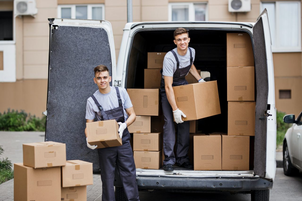 Deux déménageurs en gilet gris et gants blancs chargent des boîtes dans un camion, prêt pour le déménagement. Inclut le contexte de conseil préparation demenagement.