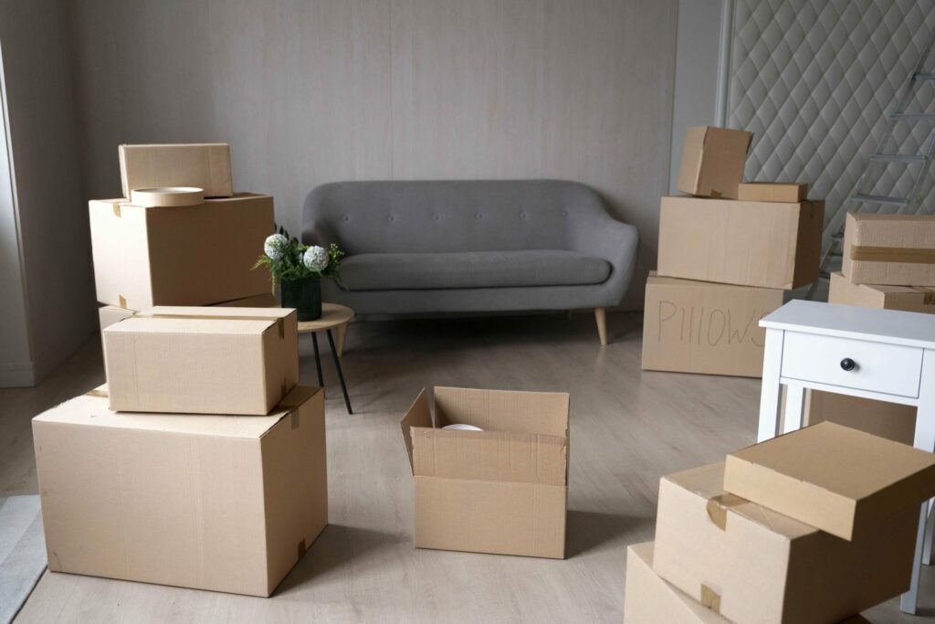 Salon lumineux avec plusieurs boîtes en carton prêtes à emballer, quelques colis ouverts et une petite table avec fleurs, prête pour un déménagement. Inclure le conseil: conseil preparation demenagement.